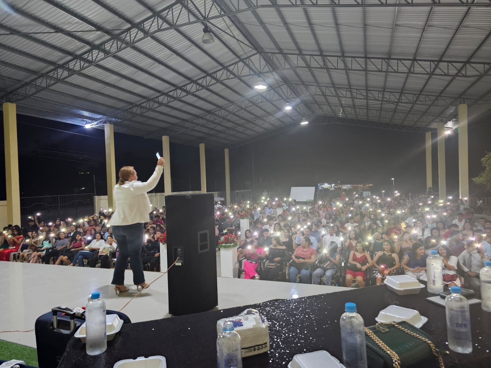 Lesly Nolasco frente a una gran audiencia durante una conferencia de LSN, con el público iluminando el lugar con las luces de sus teléfonos